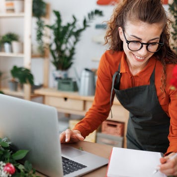 A florist/shop owner smiles as she works on a laptop