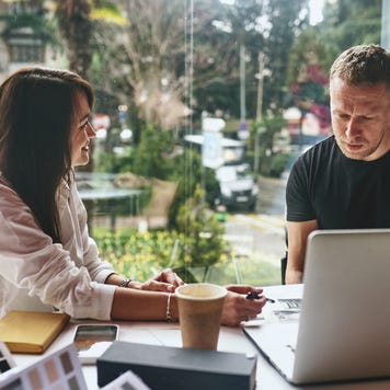 A business owner sits in her office and patiently explains something to her partner, who sits looking slightly confused.