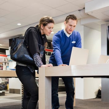 Salesman assisting female customer in buying laptop at store