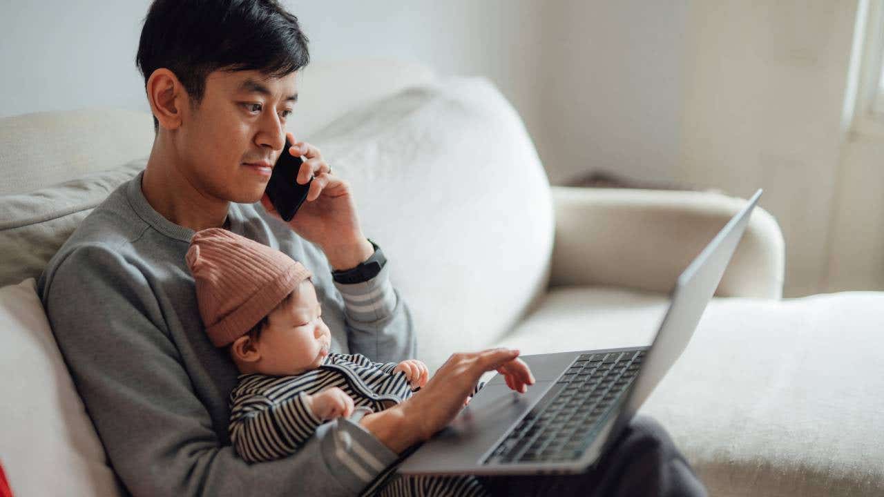 father working on laptop with daughter on his lap at home