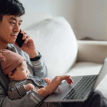 father working on laptop with daughter on his lap at home