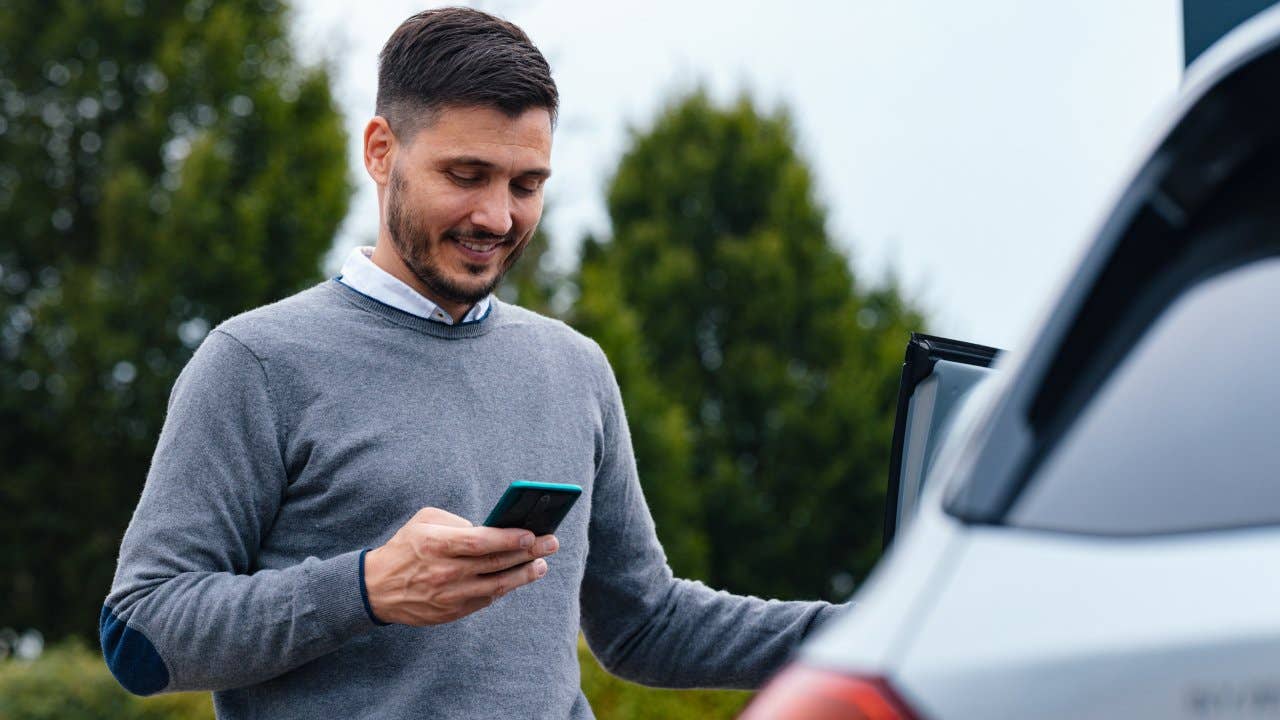 A Happy Businessman Texting On His Mobile Phone While Standing Near His Car
