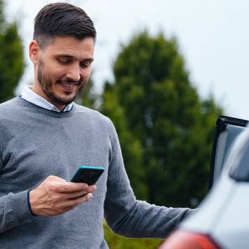 A Happy Businessman Texting On His Mobile Phone While Standing Near His Car