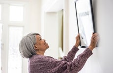 Senior woman hanging picture at home