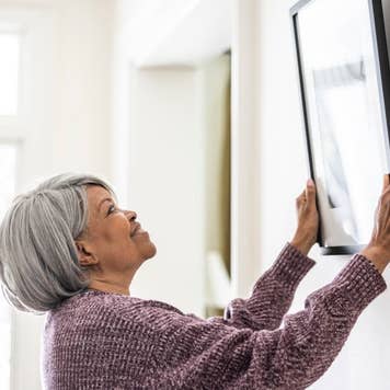 Senior woman hanging picture at home
