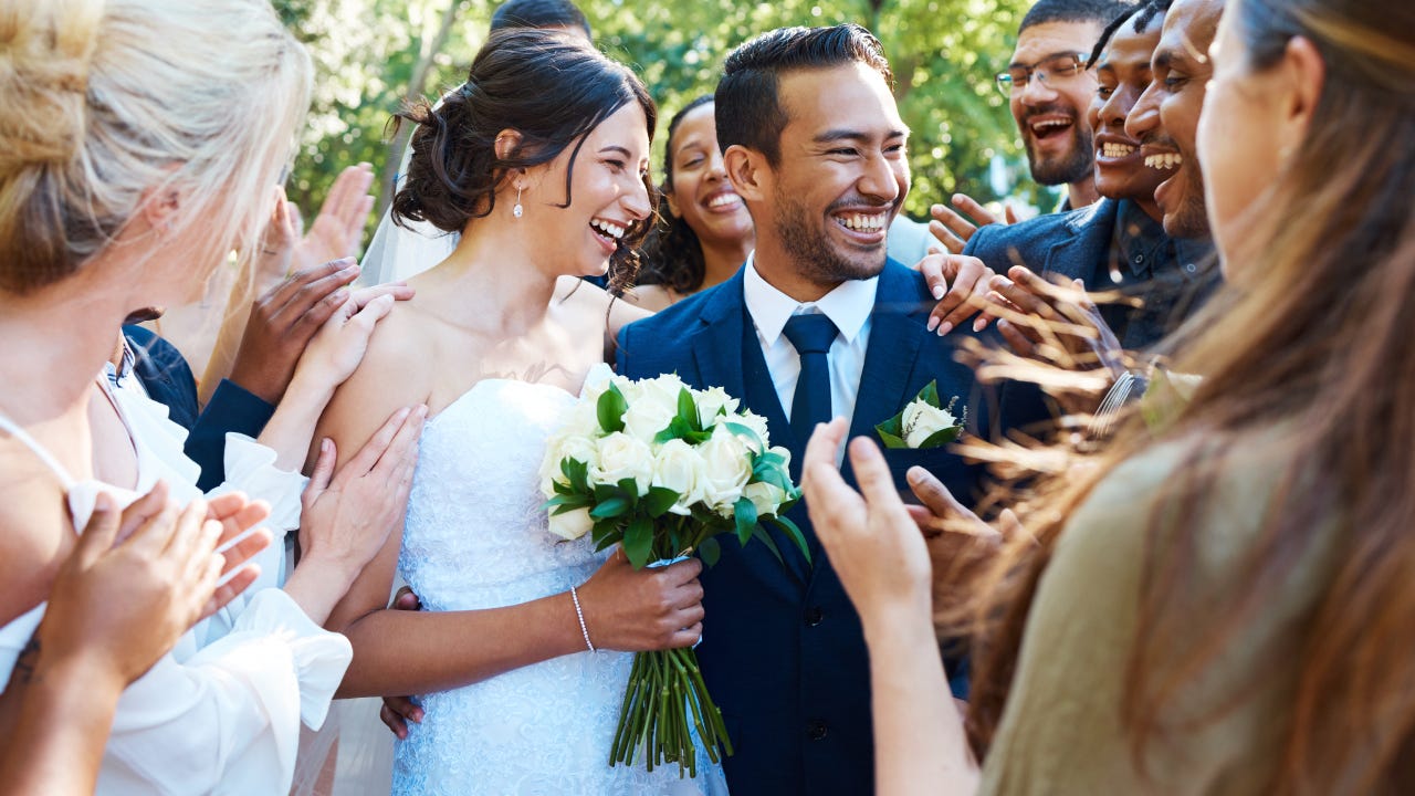 Happy bride and groom standing together while greeting guests after their wedding ceremony. Newlyweds smiling while friends and family congratulate them on their marriage