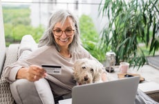 Senior woman with laptop and dog outdoors on balcony at home, making online payment.