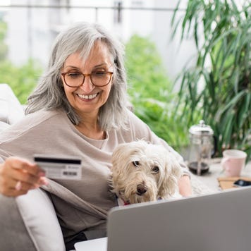 Senior woman with laptop and dog outdoors on balcony at home, making online payment.