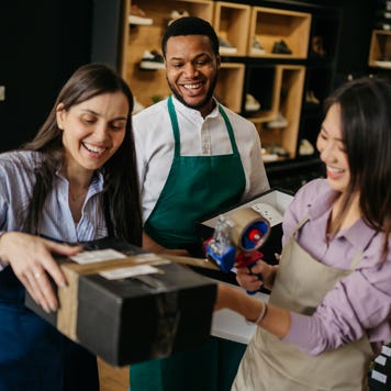 A businesswoman helps her employees package shoes for shipping.