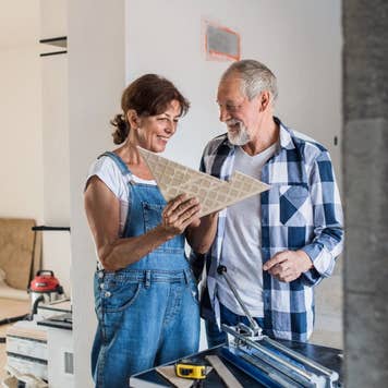 Senior couple laying tile floor in new home