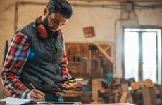 A carpenter in his workshop looks at his phone and takes notes.