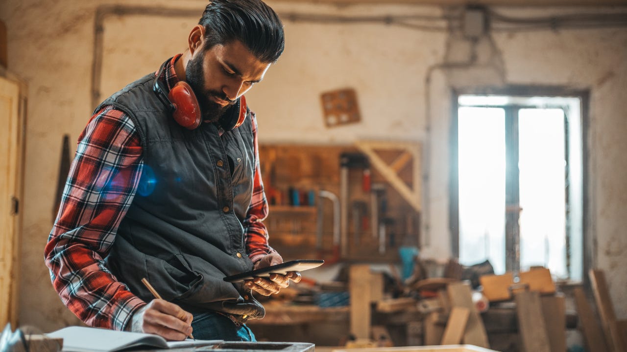 A carpenter in his workshop looks at his phone and takes notes.