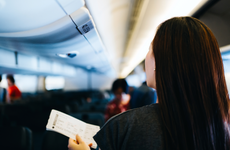 Rear view of young Asian female traveller holding her boarding pass, walking down the aisle in the airplane looking for her seat. Travel and vacation concept