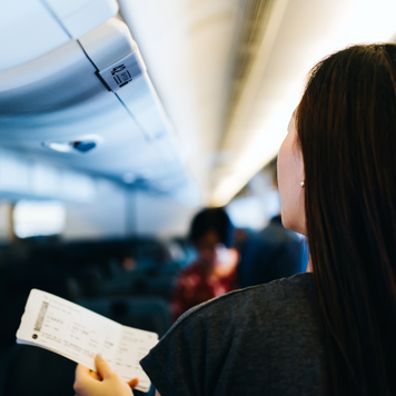 Rear view of young Asian female traveller holding her boarding pass, walking down the aisle in the airplane looking for her seat. Travel and vacation concept