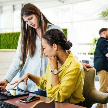 Two coworkers talking around a desk and computer