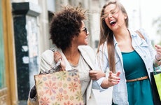 Two young woman holding shopping bags while walking on the street laughing and smiling