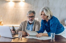 Old couple with papers and laptop on kitchen table at home