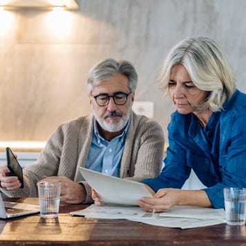 Old couple with papers and laptop on kitchen table at home