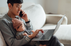Asian father working on laptop with daughter on his lap at home
