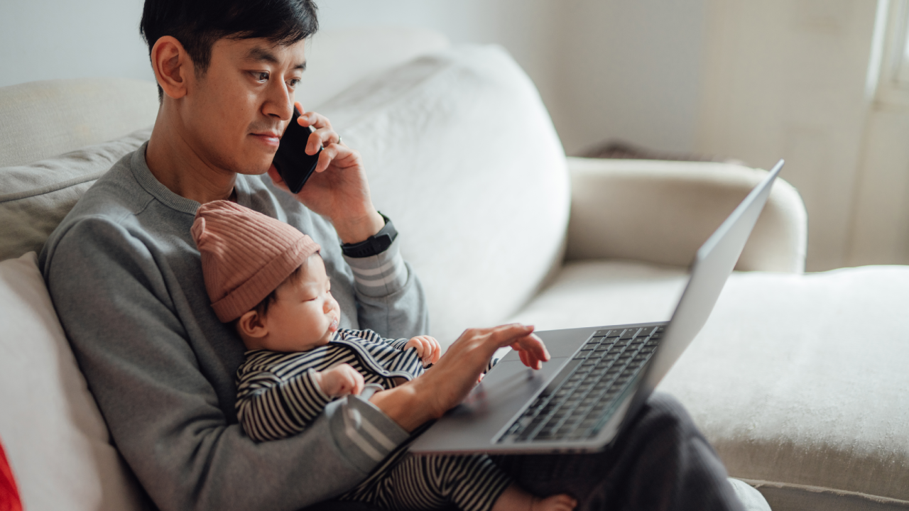 Asian father working on laptop with daughter on his lap at home