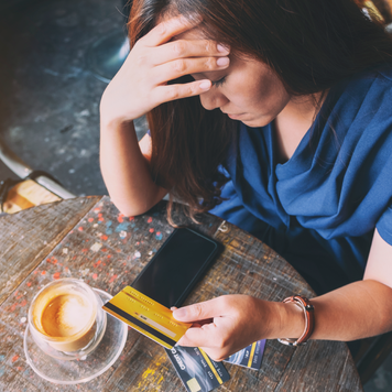 adult women looking at her credit card with one hand on her foerhead