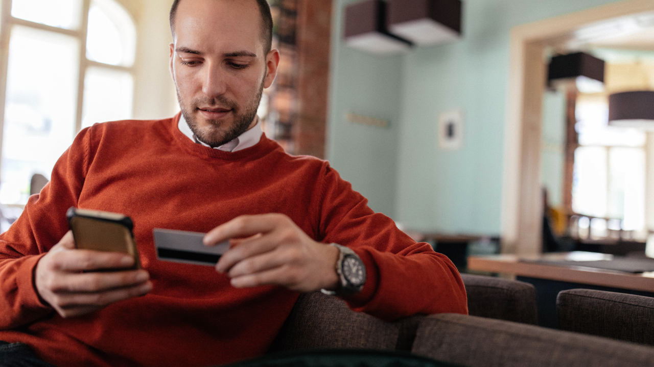 man holding his credit card and phone in his hands while sitting down