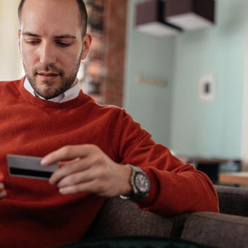 man holding his credit card and phone in his hands while sitting down