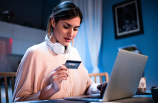 women sitting down in front of her laptop with headphones around her neck holding a credit card in her hand