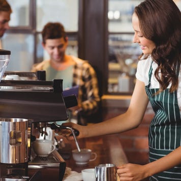 A young, smiling coffee shop owner prepares coffee for customers.