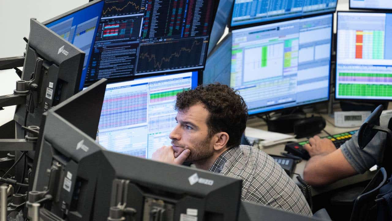 A stock trader follows the price development on his monitors in a trading room