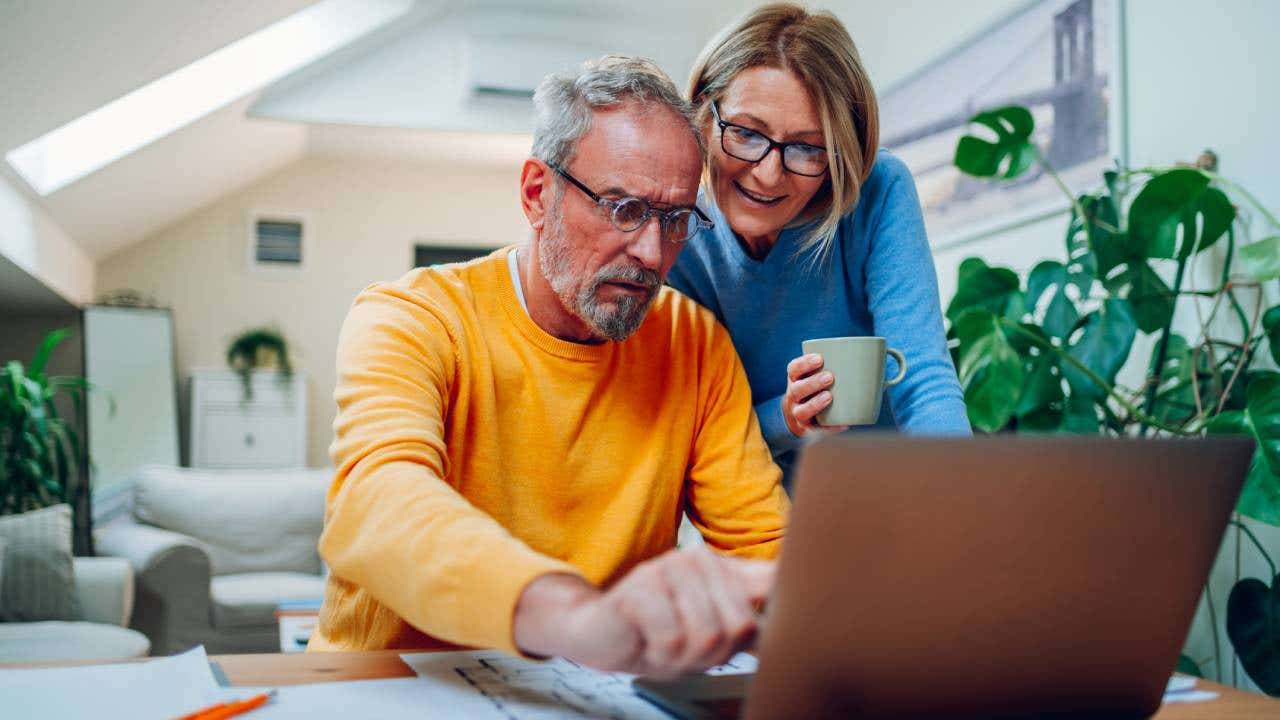 Senior middle aged happy couple using laptop together at home