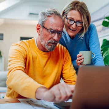 Senior middle aged happy couple using laptop together at home