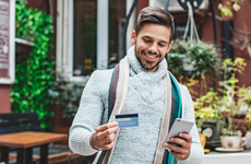A young man in warm clothing using a mobile phone and credit card