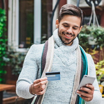 A young man in warm clothing using a mobile phone and credit card