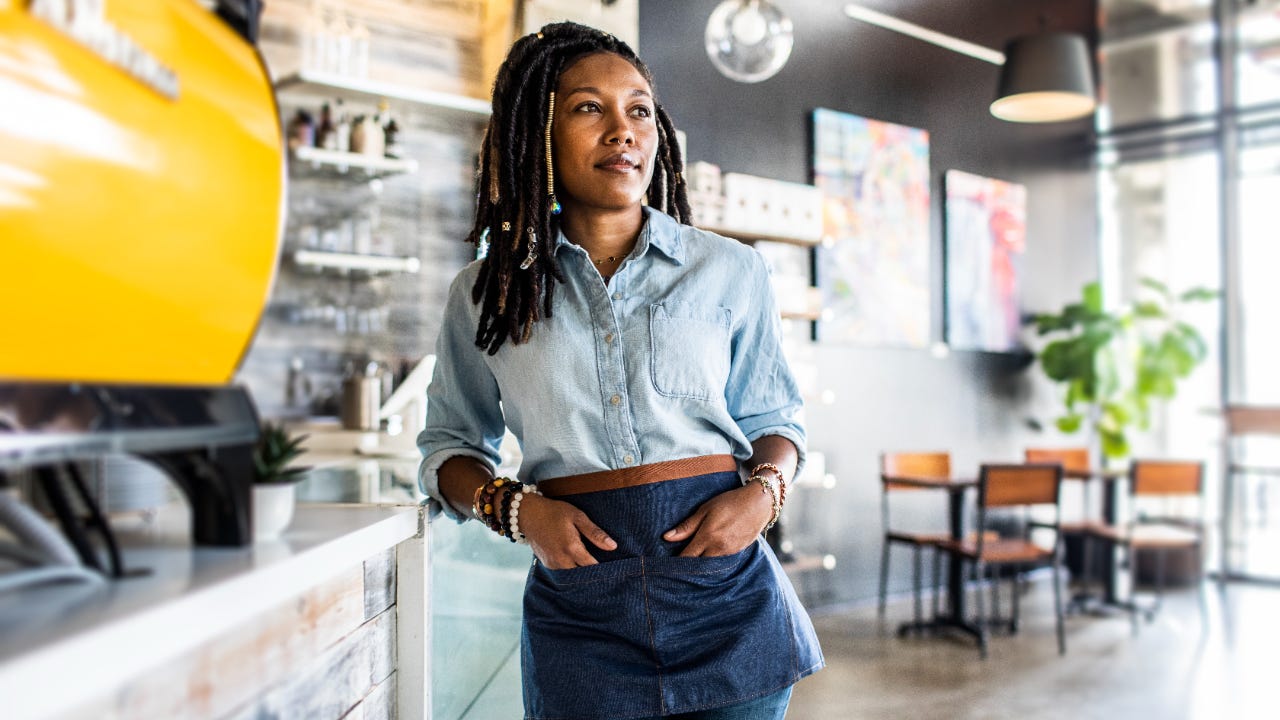 Female coffee shop owner stands in front of the counter.