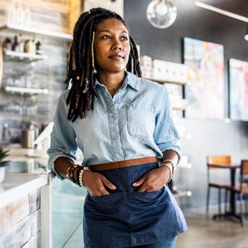 Female coffee shop owner stands in front of the counter.