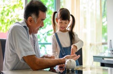 Loving Asian grandfather teaching his grandkids to save money in piggy bank