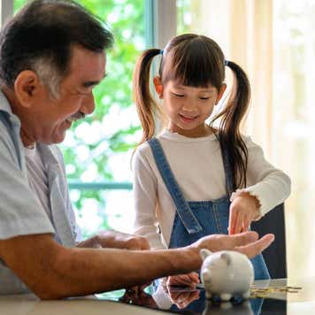 Loving Asian grandfather teaching his grandkids to save money in piggy bank