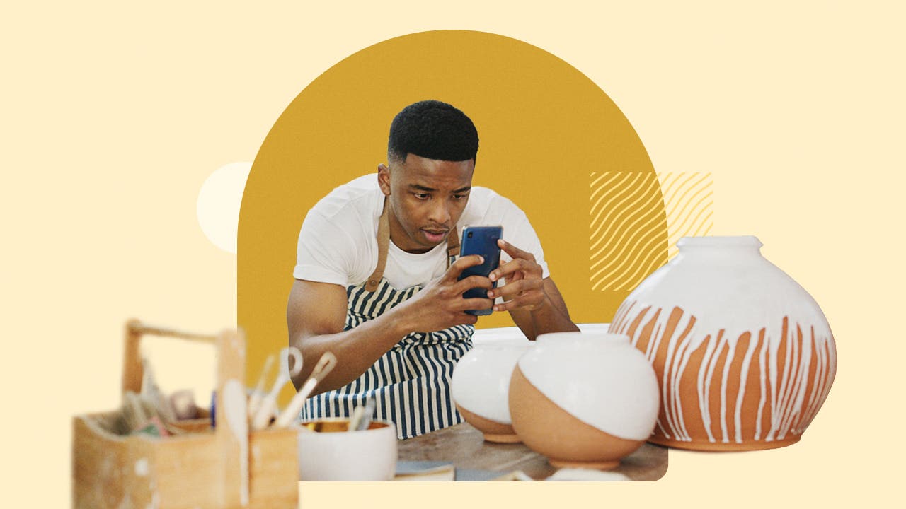 A young entrepreneur in a striped apron uses his phone to take pictures of his pottery for social media.