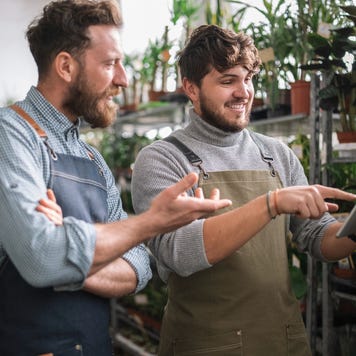 Two men in aprons look at a tablet inside a garden center.