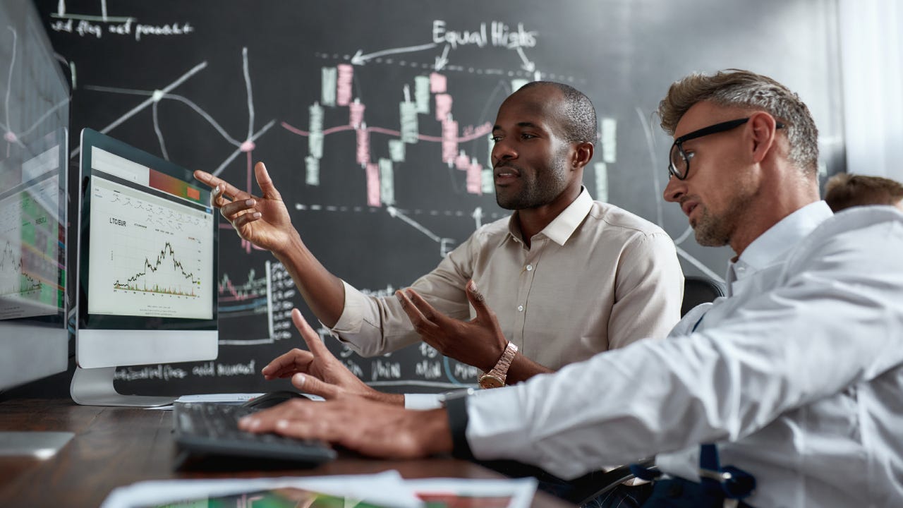 colleagues traders discussing ideas while sitting in the office in front of multiple computer screens