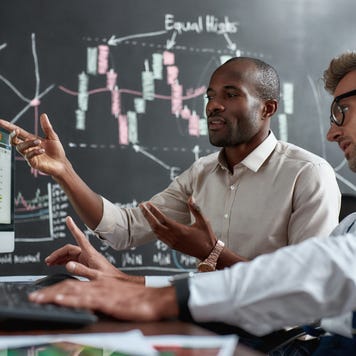 colleagues traders discussing ideas while sitting in the office in front of multiple computer screens