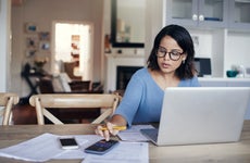 Image of a young woman using a laptop and calculator while working from home