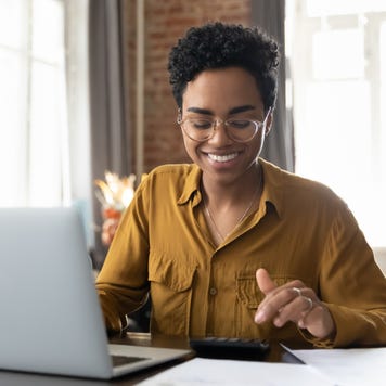 woman in glasses counting profit, on calculator at laptop computer