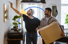 Two men standing together inside a house. One is holding a box.