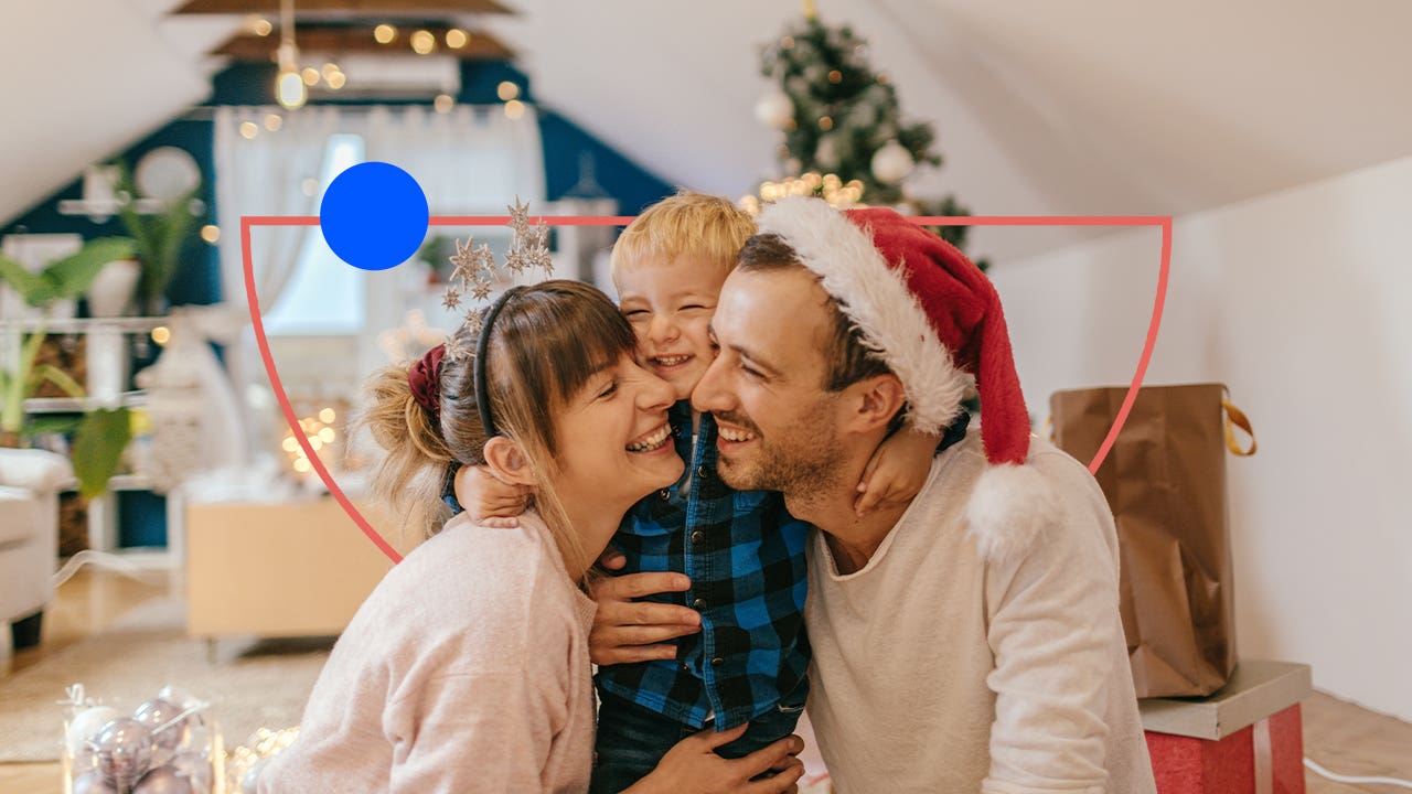 A young couple with child gathered around and laughing in front of a Christmas tree