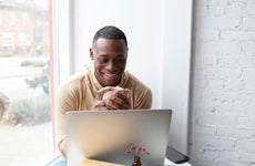 Man sitting at cafe table holding coffee cup and looking at laptop, smiling