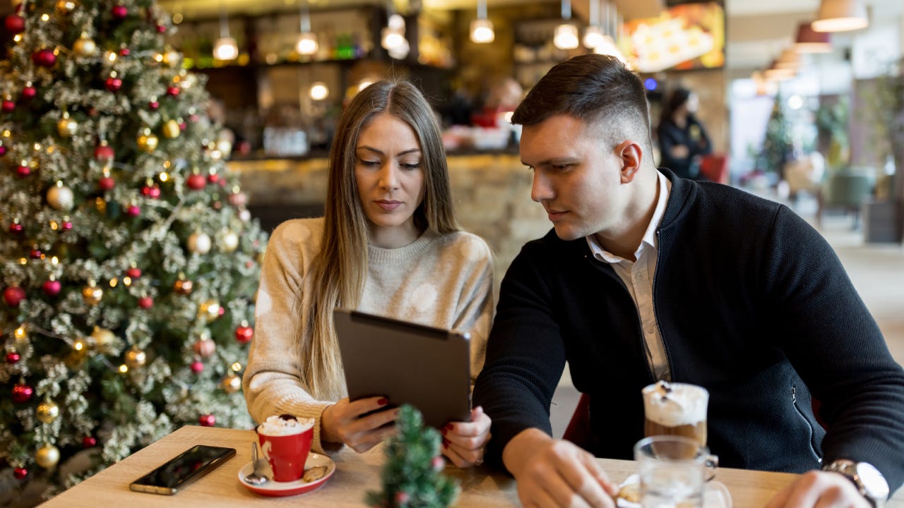 Young couple enjoying hot chocolate and using digital tablet in restaurant during Christmas holidays