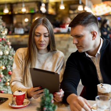 Young couple enjoying hot chocolate and using digital tablet in restaurant during Christmas holidays