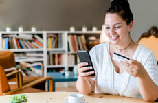 Smiling woman with coffee on table doing online shopping over mobile phone in cafe - stock photo